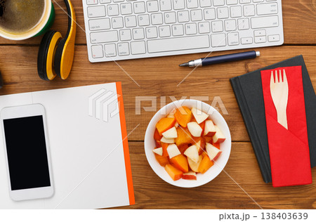 Healthy lunch at workplace. Top view flat lay of desktop fruit snack in foil container and mobile phone on wooden desk background 138403639