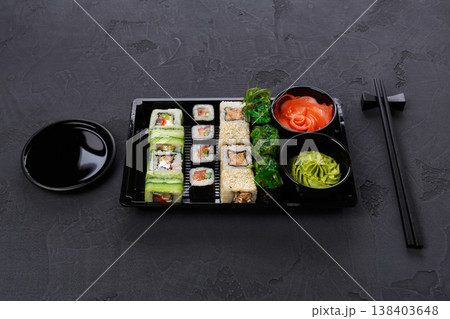 Japanese restaurant delivery, take away box pov, sushi maki and roll set. Chopsticks, ginger, soy sauce, wasabi. Meals at black background 138403648