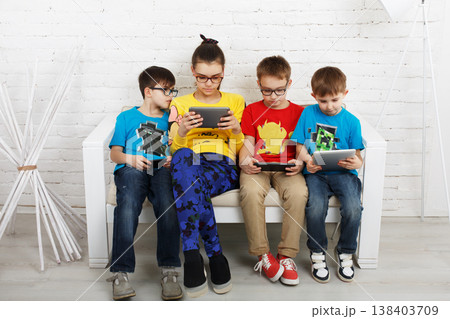 Group of kids in eye glasses look into their phones and tablets. Children computer games, social networks and media addiction concept. Girl and boys with tablet and smartphones. Communication problems 138403709