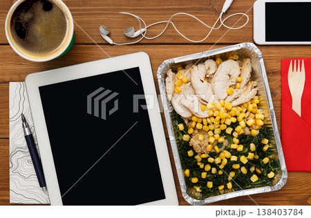 Healthy business lunch at workplace. Top view flat lay of desktop - tablet pc with copy space and phone on wooden desk background with snack in foil container Healthy business lunch at workplace. Top view flat lay of desktop - tablet pc with copy space and phone on wooden desk background with snack in foil container 138403784