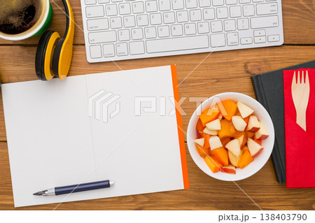 Healthy lunch at workplace. Top view with copy space, flat lay of desktop fruit snack in foil container on wooden desk background Healthy lunch at workplace. Top view with copy space, flat lay of desktop fruit snack in foil container on wooden desk background 138403790