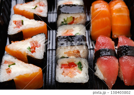 Japanese food restaurant delivery. Sushi maki and roll set closeup in black takeaway box, seafood background Japanese food restaurant delivery. Sushi maki and roll set closeup in black takeaway box, seafood background 138403802