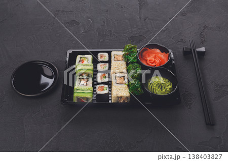 Japanese restaurant delivery, take away box top view, sushi maki and roll set. Chopsticks, ginger, soy sauce, wasabi. Meals at black background Japanese restaurant delivery, take away box top view, sushi maki and roll set. Chopsticks, ginger, soy sauce, wasabi. Meals at black background 138403827