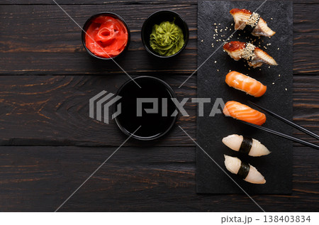 Eating sushi. Japanese food restaurant, unagi and salmon sushi on dark background. Taking piece with chopsticks. Top view on black wood 138403834
