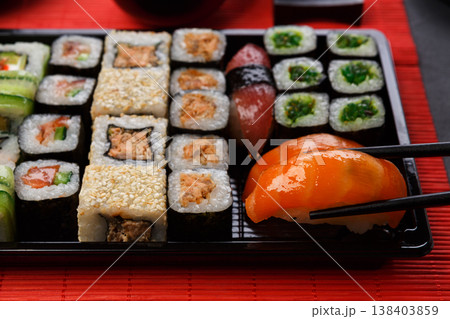 Eating salmon sushi. Japanese food restaurant, sushi maki and roll plate or platter set. Closeup of hand with chopsticks taking roll. Eating salmon sushi. Japanese food restaurant, sushi maki and roll plate or platter set. Closeup of hand with chopsticks taking roll. 138403859