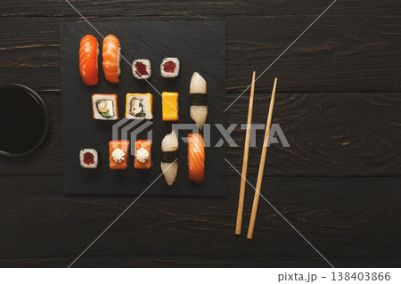 Japanese food restaurant, sushi and rolls on dark background. Set with chopsticks and soy sauce. Top view on black wood, copy space 138403866
