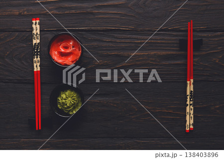 Pieces of traditional japanese tablewear. Red chopsticks with hierogliphs, small black bowls with ginger and wasabi on dark wooden table. Top view, flat lay, copy space, background Pieces of traditional japanese tablewear. Red chopsticks with hierogliphs, small black bowls with ginger and wasabi on dark wooden table. Top view, flat lay, copy space, background 138403896