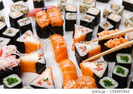 Japanese food restaurant delivery closeup - sushi and rolls platter set isolated at white background with wooden chopsticks taking one piece Japanese food restaurant delivery closeup - sushi and rolls platter set isolated at white background with wooden chopsticks taking one piece 138403942