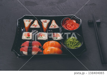 Japanese food restaurant delivery, take away box, sushi maki and roll set. Chopsticks, ginger, soy sauce, wasabi. Meals at black background Japanese food restaurant delivery, take away box, sushi maki and roll set. Chopsticks, ginger, soy sauce, wasabi. Meals at black background 138404065