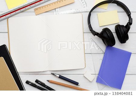 Stationery supplies in modern office workspace. Top view on open blank notebook, pen, pencil, rulers, small notepads and memo pads, headphones on white wooden desktop, flat lay, copy space, mockup Stationery supplies in modern office workspace. Top view on open blank notebook, pen, pencil, rulers, small notepads and memo pads, headphones on white wooden desktop, flat lay, copy space, mockup 138404081