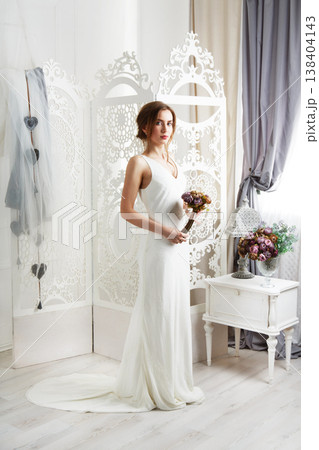 Wedding dress fashion. Beautiful young bride in vintage wedding dress indoors. White wedding dress at model. Girl shows wedding fashion in decorated shabby chic interior with flowers, high key. Wedding dress fashion. Beautiful young bride in vintage wedding dress indoors. White wedding dress at model. Girl shows wedding fashion in decorated shabby chic interior with flowers, high key. 138404143