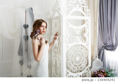 Wedding dress fashion. Beautiful young bride in vintage wedding dress indoors. White wedding dress at model. Girl shows wedding fashion in decorated shabby chic interior with flowers, high key. Wedding dress fashion. Beautiful young bride in vintage wedding dress indoors. White wedding dress at model. Girl shows wedding fashion in decorated shabby chic interior with flowers, high key. 138404241