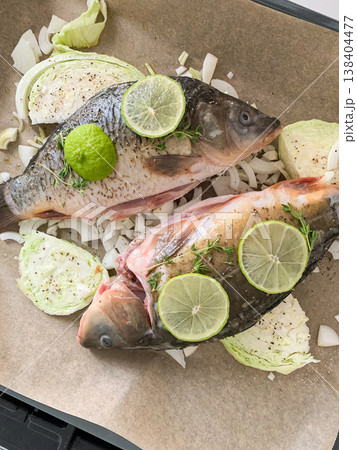 Fish is placed in an oven tray alongside fresh cabbage slices and topped with lemon and herbs. Heat from the oven cooks the meal inside the kitchen for dinner Fish is placed in an oven tray alongside fresh cabbage slices and topped with lemon and herbs. Heat from the oven cooks the meal inside the kitchen for dinner 138404477