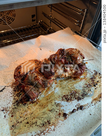 Turkey meat is placed in the oven on a baking tray lined with paper. The tray has grease and cooking residue from the turkey. Herbs are visible on the meat 138404500
