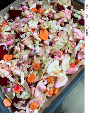 Vegetables including carrots, beets, and garlic are prepared on a baking tray ready to bake in the oven. The tray is lined and set on a stove surface 138404536
