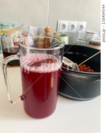 A large clear pitcher filled with a red liquid sits on a kitchen counter near a black bowl containing fruit. The scene depicts a time of cooking in the afternoon A large clear pitcher filled with a red liquid sits on a kitchen counter near a black bowl containing fruit. The scene depicts a time of cooking in the afternoon 138404544