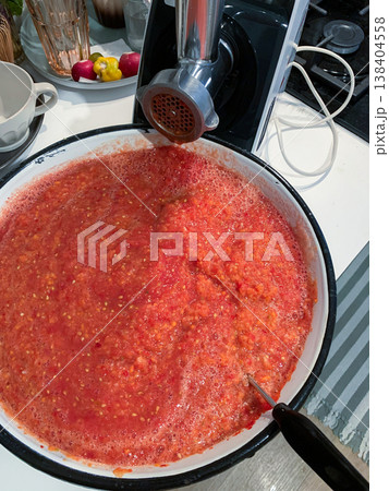 Tomatoes are being ground into a thick sauce in a kitchen. A food grinder is set up on the counter. Other colorful ingredients are on display Tomatoes are being ground into a thick sauce in a kitchen. A food grinder is set up on the counter. Other colorful ingredients are on display 138404558