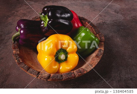 A collection of colorful bell peppers, in a wooden bowl, on a dark surface, top view, no people A collection of colorful bell peppers, in a wooden bowl, on a dark surface, top view, no people 138404585