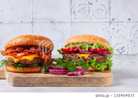 two burgers with beef patty, fried bacon, cheddar cheese, tomatoes, on a light table, two burgers with beef patty, fried bacon, cheddar cheese, tomatoes, on a light table, 138404635