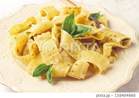 Fresh papardelle pasta, with basil and pesto sauce, is served, on a white plate, with a fork held by hand Fresh papardelle pasta, with basil and pesto sauce, is served, on a white plate, with a fork held by hand 138404660