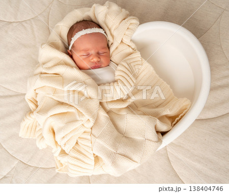 Newborn baby sleeping in a soft round nest, wrapped in beige knit fabric. Minimal newborn photography with warmth, comfort and peaceful family atmosphere Newborn baby sleeping in a soft round nest, wrapped in beige knit fabric. Minimal newborn photography with warmth, comfort and peaceful family atmosphere 138404746