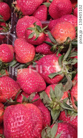 Fresh red strawberries piled together in a clear plastic container, showcasing vibrant color and natural texture, ready for sale at a market or grocery store Fresh red strawberries piled together in a clear plastic container, showcasing vibrant color and natural texture, ready for sale at a market or grocery store 138405102