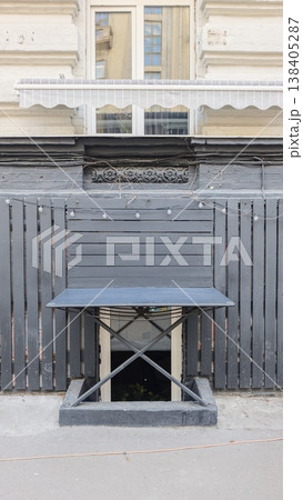 Black folding table with crossed legs positioned against a wooden fence, featuring a window with white curtains above and decorative molding on the wall 138405287