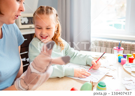A Caucasian woman and her daughter decorate paper bunny masks at the table, enjoying creative Easter preparation and family bonding. Mid shot A Caucasian woman and her daughter decorate paper bunny masks at the table, enjoying creative Easter preparation and family bonding. Mid shot 138407437
