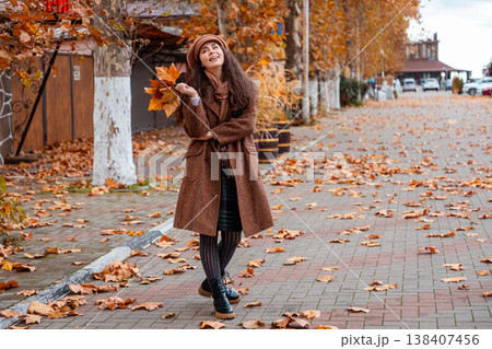 A young Caucasian woman in a fashionable coat walks slowly through quiet urban streets, appreciating the charm of the season and her relaxed weekend moment. Wide shot A young Caucasian woman in a fashionable coat walks slowly through quiet urban streets, appreciating the charm of the season and her relaxed weekend moment. Wide shot 138407456
