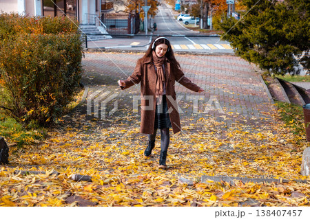 Wide shot of a happy young Caucasian woman in a coat listening to music with headphones and dancing in park. Top view. Concept of happiness and freedom Wide shot of a happy young Caucasian woman in a coat listening to music with headphones and dancing in park. Top view. Concept of happiness and freedom 138407457