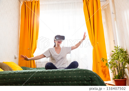 Woman sitting on a comfortable bed enjoying the latest VR technology, interacting with advanced AI algorithms. Wide shot, bottom view Woman sitting on a comfortable bed enjoying the latest VR technology, interacting with advanced AI algorithms. Wide shot, bottom view 138407502