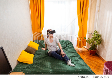 Woman interacting with virtual reality spaces while sitting on bed, embracing the evolution of digital entertainment. Wide shot, top view 138407505