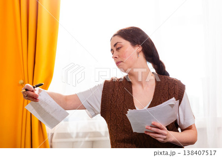 Portrait of thoughtful young woman checking invoices, sitting on bed, and planning home budget. Economy and financial planning. Side view 138407517