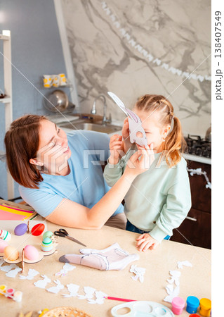 A beautiful family moment as a mother and her daughter wear Easter bunny masks at home, enjoying playful crafting time before the holiday celebration. Vertical A beautiful family moment as a mother and her daughter wear Easter bunny masks at home, enjoying playful crafting time before the holiday celebration. Vertical 138407549