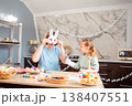 A young Caucasian mother and her daughter wear handmade bunny masks at home, smiling and playing at the table while getting ready for Easter together with joy and creativity. Wide shot 138407551