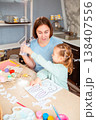 A Caucasian woman and her daughter craft holiday ornaments together, cutting decorations at the table and celebrating Easter traditions with children. Vertical 138407556