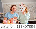 A bright Easter preparation scene with a young mother and her daughter wearing handmade bunny masks while sitting at the table and having fun at home. Bottom view 138407559