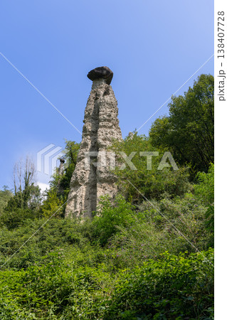 Low angle view of giant capped hoodoo at the Pyramids of Zone with pale tower and blue sky in Italy 138407728