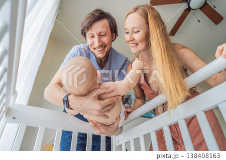 Mother and father lifting baby from crib and holding in arms at home. Loving parents caring for newborn together. Family bonding, parenthood, tenderness and emotional connection concept 138408163