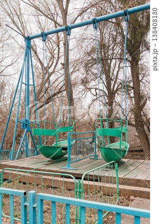 Vintage Blue and Green Swing Set in Abandoned Park with Bare Trees and Weathered Wooden Platform Showing Signs of Decay Vintage Blue and Green Swing Set in Abandoned Park with Bare Trees and Weathered Wooden Platform Showing Signs of Decay 138408180