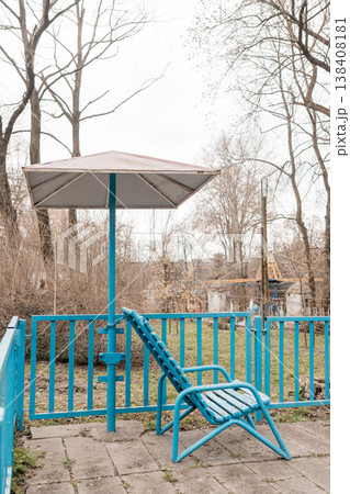 Vintage Blue Patio Chair Under Umbrella on Concrete Terrace Amidst Bare Trees in Overcast Outdoor Setting 138408181