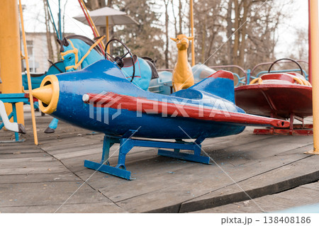 Vintage Blue and Red Airplane Carousel Ride at Outdoor Amusement Park With Wooden Deck and Colorful Animal Figures Vintage Blue and Red Airplane Carousel Ride at Outdoor Amusement Park With Wooden Deck and Colorful Animal Figures 138408186
