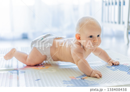 Baby lying on play mat learning to crawl and get on all fours. Infant practicing motor skills and development at home. Early childhood growth, milestones and active learning concept Baby lying on play mat learning to crawl and get on all fours. Infant practicing motor skills and development at home. Early childhood growth, milestones and active learning concept 138408438