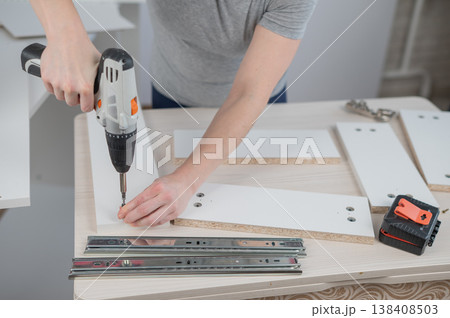 A Caucasian woman uses a screwdriver to tighten a screw while assembling a cabinet. 138408503