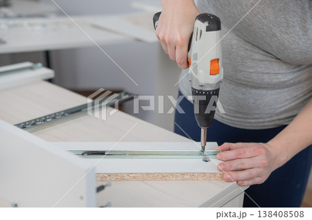 A Caucasian woman uses a screwdriver to tighten a screw while assembling a cabinet. 138408508