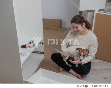 A Caucasian woman assembles furniture with her cute dog. A Caucasian woman assembles furniture with her cute dog. 138408514