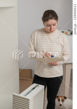 A Caucasian woman looks at the assembly instructions for a wardrobe with confusion. A Caucasian woman looks at the assembly instructions for a wardrobe with confusion. 138408521