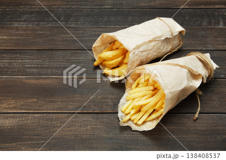 Tasty potato wedges and french fries wrapped into brown kraft wrapping paper. Fast food take away at rustic wooden boards background. Choice of fried potatoes at wood. Chips, potato slices. Top view 138408537