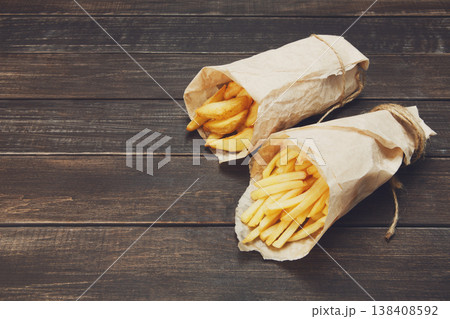 Tasty potato wedges and french fries wrapped into brown kraft wrapping paper. Fast food take away at rustic wood background. Choice of fried potatoes at wood. Chips, potato slices. Top view, copyspace Tasty potato wedges and french fries wrapped into brown kraft wrapping paper. Fast food take away at rustic wood background. Choice of fried potatoes at wood. Chips, potato slices. Top view, copyspace 138408592