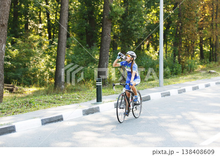 Female sportsman cyclist drinks water from the bottle at the race. Riding racing bicycle. Break, stop at road. Woman cycling on countryside summer road or highway. Triathlon or cycling competition. 138408609